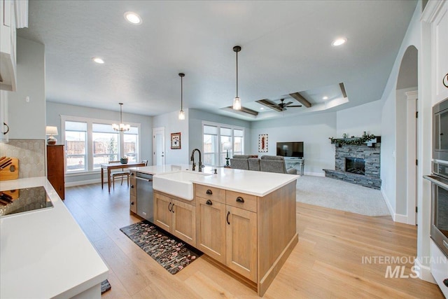 kitchen with light wood-type flooring, a sink, light brown cabinets, appliances with stainless steel finishes, and a stone fireplace