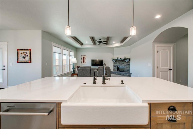 kitchen featuring open floor plan, stainless steel dishwasher, a raised ceiling, a sink, and ceiling fan