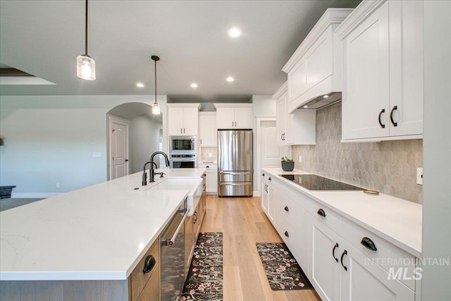 kitchen featuring a sink, backsplash, a large island, light wood-style flooring, and stainless steel appliances