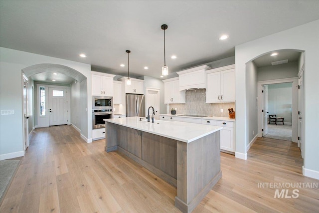 kitchen featuring light countertops, white cabinets, light wood finished floors, appliances with stainless steel finishes, and arched walkways