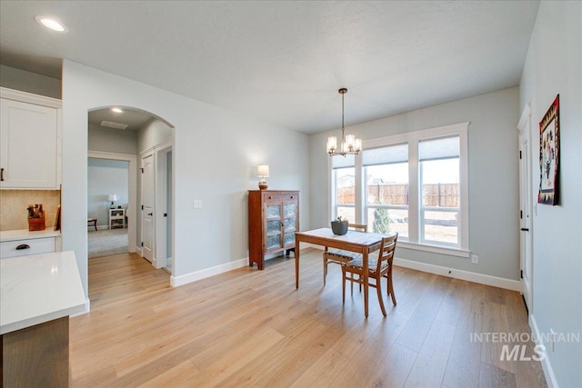 dining room with arched walkways, baseboards, a notable chandelier, and light wood-type flooring