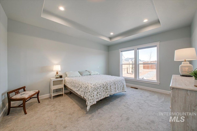 bedroom featuring baseboards, a tray ceiling, visible vents, and light carpet