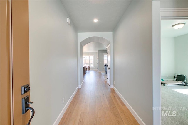 hallway featuring recessed lighting, arched walkways, baseboards, and light wood-type flooring