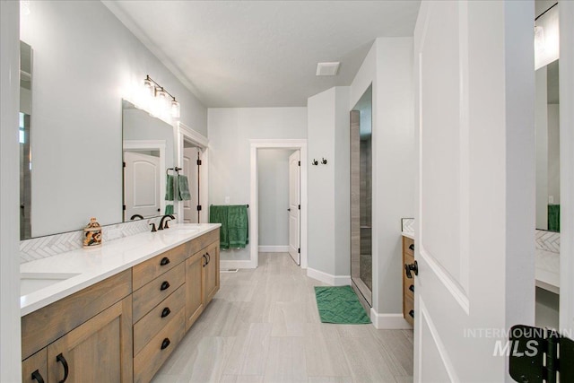 bathroom with baseboards, double vanity, a sink, and a shower stall