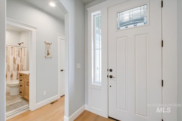 foyer entrance featuring baseboards, light wood-type flooring, visible vents, and arched walkways
