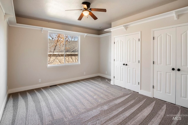 unfurnished bedroom with carpet flooring, ceiling fan, and two closets