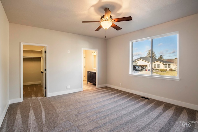 unfurnished bedroom featuring carpet, a walk in closet, ensuite bathroom, ceiling fan, and a closet