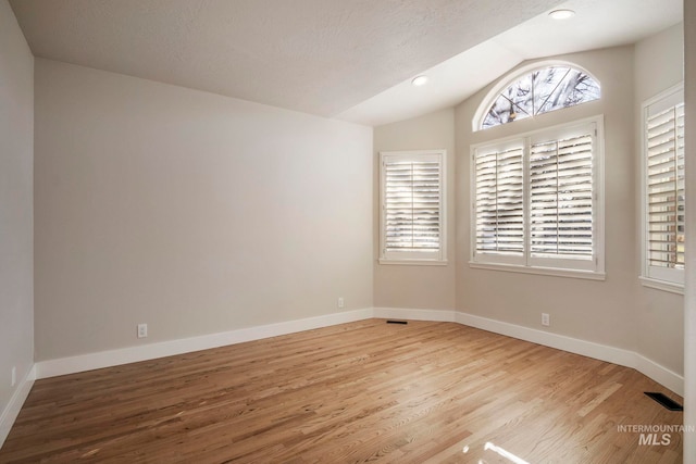 empty room featuring a textured ceiling, hardwood / wood-style floors, and lofted ceiling