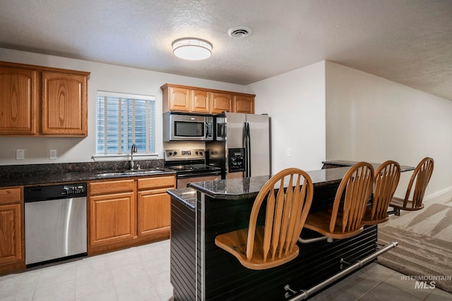 kitchen with sink, dark stone counters, a textured ceiling, and appliances with stainless steel finishes