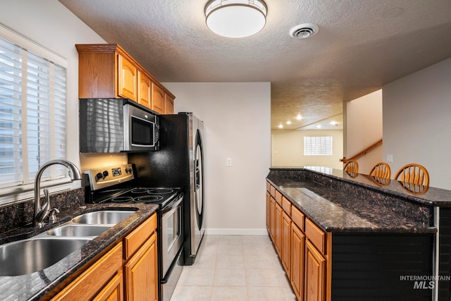 kitchen with dark stone counters, sink, stainless steel appliances, and a textured ceiling