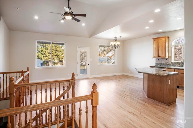 kitchen with backsplash, vaulted ceiling, a kitchen island, light stone countertops, and light hardwood / wood-style floors