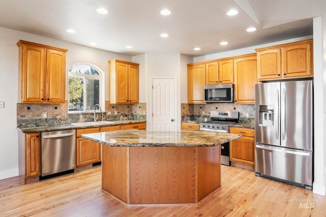 kitchen featuring sink, light hardwood / wood-style flooring, dark stone counters, a kitchen island, and appliances with stainless steel finishes