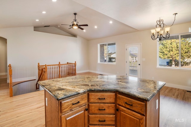 kitchen featuring ceiling fan with notable chandelier, a center island, light wood-type flooring, and dark stone counters