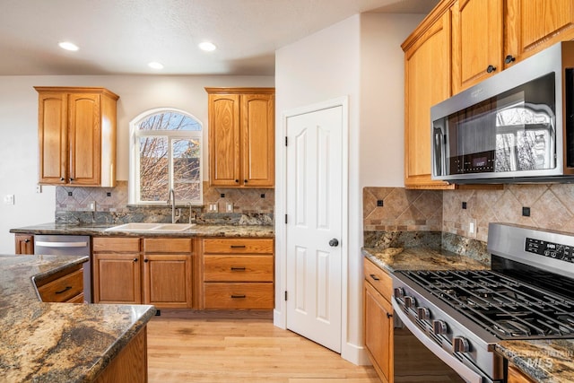 kitchen featuring sink, light hardwood / wood-style flooring, backsplash, dark stone countertops, and appliances with stainless steel finishes