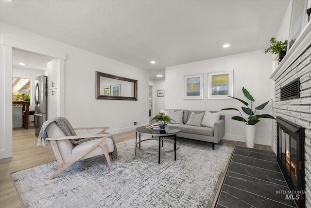living area with a stone fireplace, light wood-type flooring, recessed lighting, and baseboards