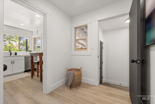 hall featuring a sink, light wood-type flooring, baseboards, and recessed lighting