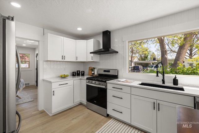 kitchen with appliances with stainless steel finishes, wall chimney exhaust hood, a sink, light countertops, and recessed lighting