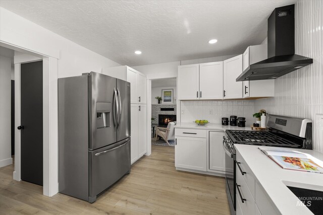 kitchen with appliances with stainless steel finishes, wall chimney range hood, light countertops, recessed lighting, and light wood-style flooring