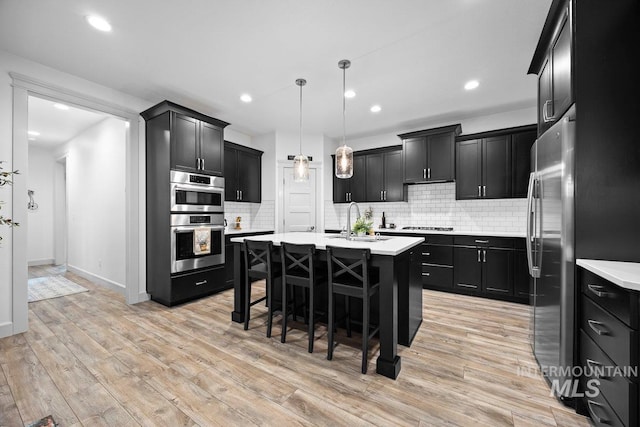 kitchen featuring a center island with sink, light countertops, hanging light fixtures, a sink, and dark cabinetry