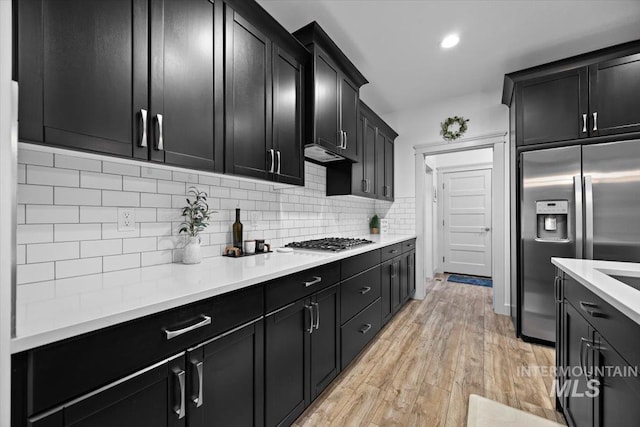 kitchen featuring dark cabinets, light countertops, appliances with stainless steel finishes, light wood-type flooring, and backsplash