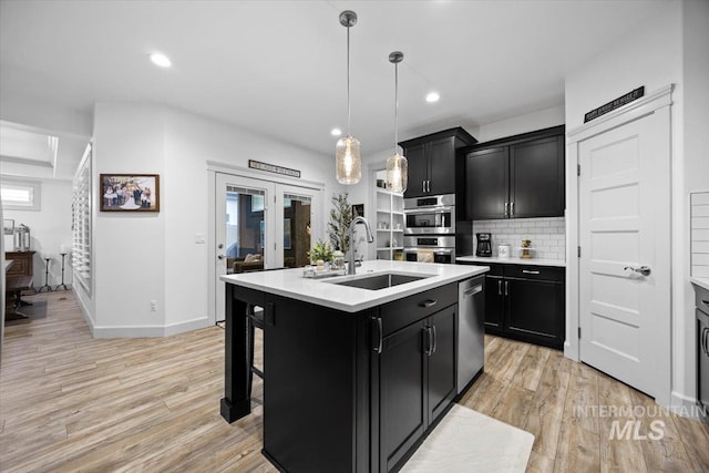 kitchen with a sink, a center island with sink, light countertops, and dark cabinets