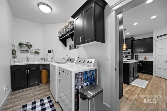 clothes washing area featuring cabinet space, light wood-style floors, washing machine and dryer, a sink, and baseboards