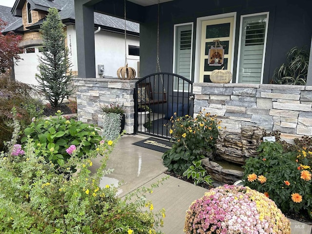 property entrance with a garage, a shingled roof, stone siding, a gate, and stucco siding