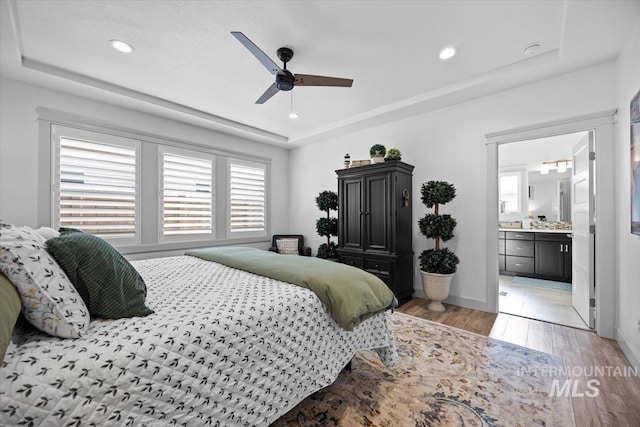 bedroom featuring light wood-type flooring, ensuite bath, a tray ceiling, and recessed lighting