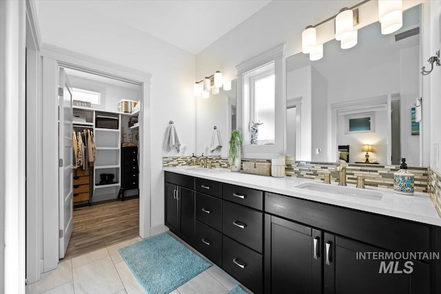 full bathroom featuring double vanity, backsplash, a walk in closet, and a sink