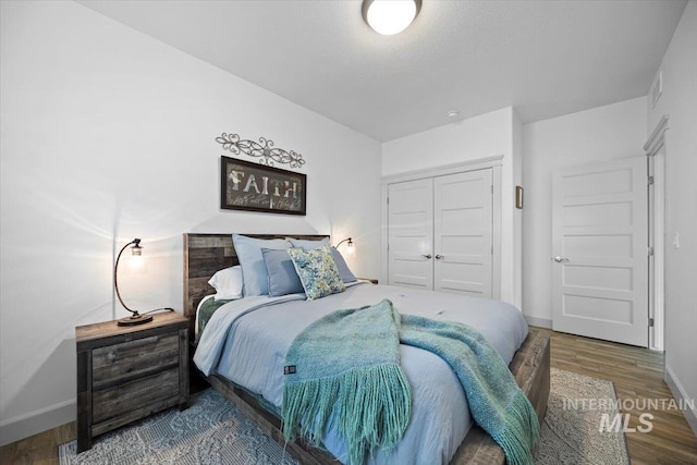 bedroom featuring a closet, wood finished floors, visible vents, and baseboards