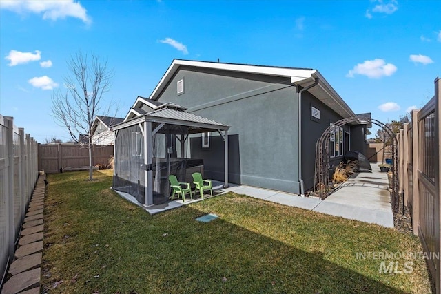 rear view of property featuring a gazebo, a lawn, a fenced backyard, and stucco siding