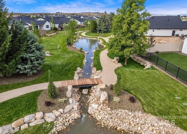 view of property's community featuring a lawn, a water view, fence, and a residential view