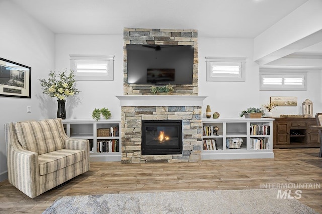 living area with plenty of natural light, a stone fireplace, and wood finished floors