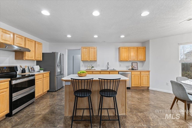 kitchen featuring a sink, under cabinet range hood, appliances with stainless steel finishes, a kitchen bar, and a center island