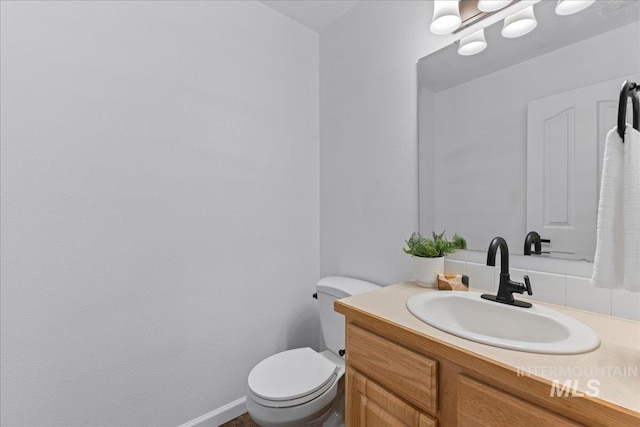 half bathroom with vanity, toilet, and baseboards