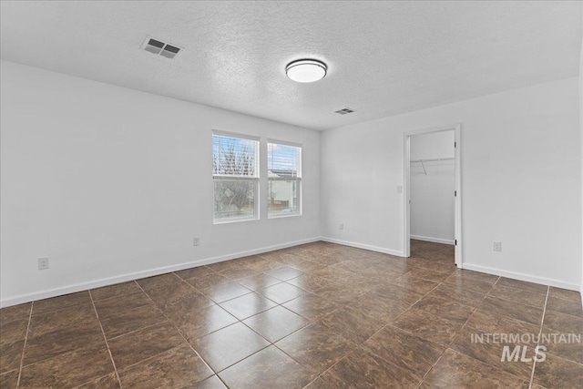 spare room featuring visible vents, a textured ceiling, and baseboards