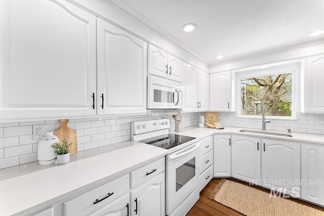 kitchen with a sink, white appliances, light countertops, white cabinetry, and backsplash