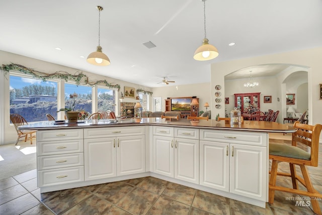 kitchen with pendant lighting, ceiling fan with notable chandelier, and white cabinetry