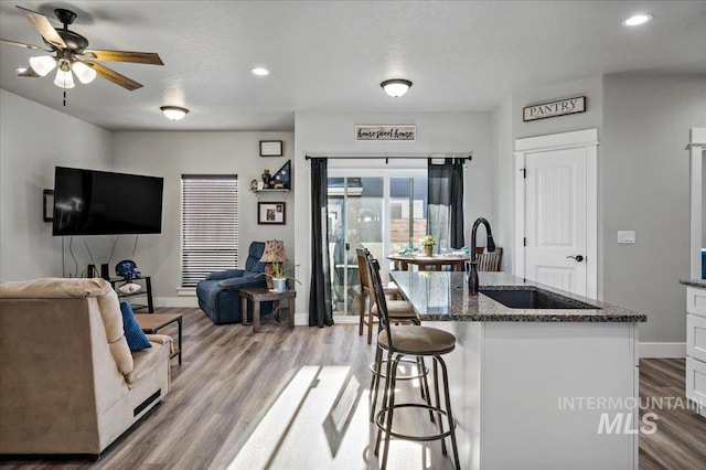 kitchen featuring ceiling fan, sink, a kitchen breakfast bar, dark stone counters, and white cabinets