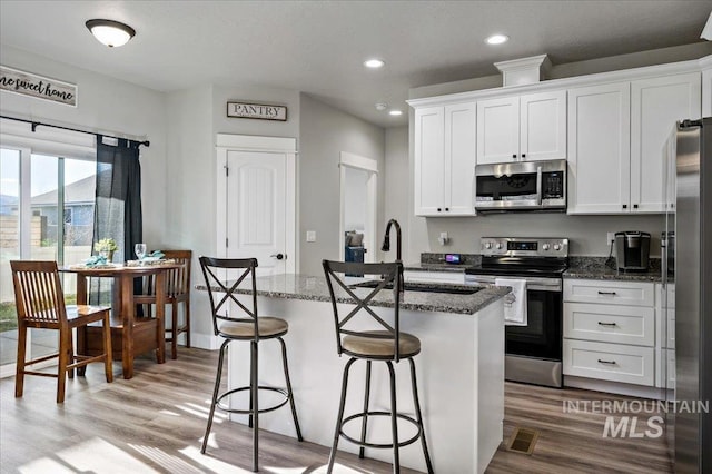 kitchen featuring white cabinets, appliances with stainless steel finishes, dark stone countertops, and an island with sink