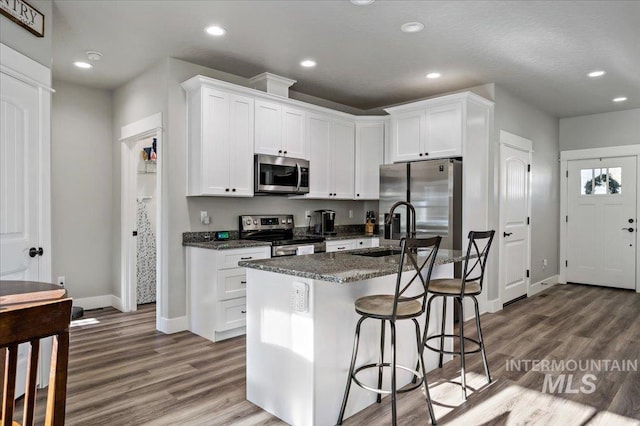 kitchen with white cabinets, sink, stainless steel appliances, and an island with sink