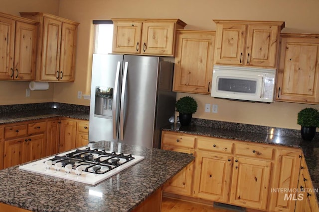 kitchen with dark stone counters, light brown cabinetry, and white appliances