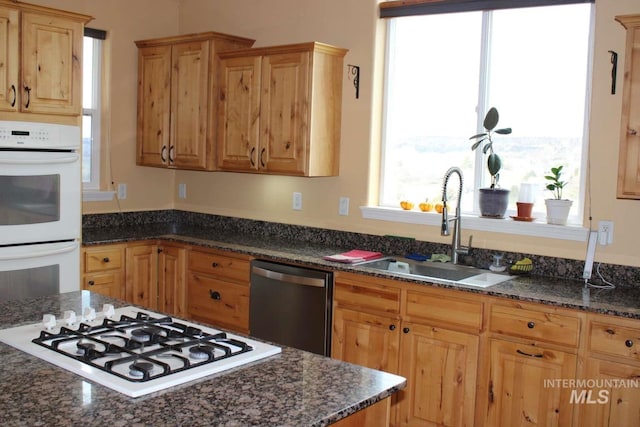 kitchen featuring white appliances, a sink, and dark stone counters