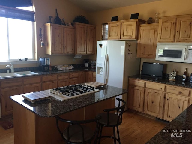 kitchen with light wood finished floors, a sink, dark stone counters, and white appliances