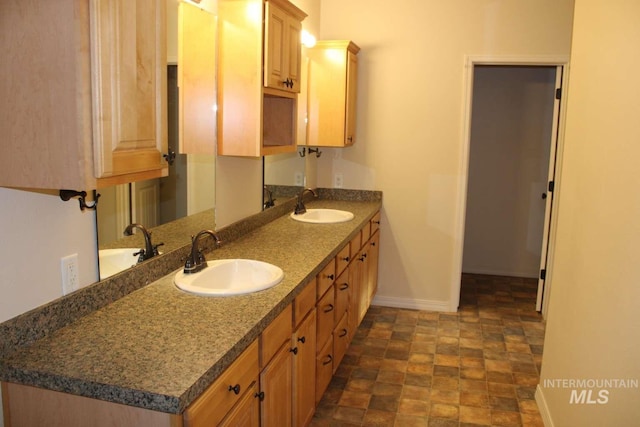 full bath featuring double vanity, a sink, stone finish flooring, and baseboards