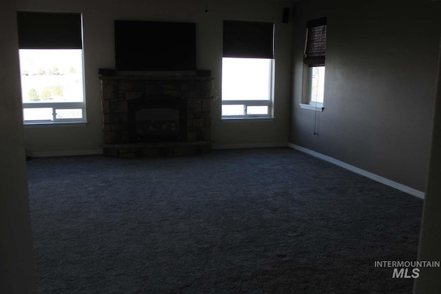 unfurnished living room with a stone fireplace, baseboards, and carpet flooring