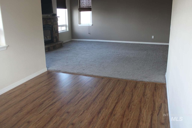 carpeted empty room featuring baseboards, a fireplace, and wood finished floors