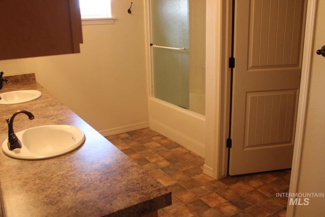 bathroom featuring enclosed tub / shower combo, a sink, stone finish flooring, and baseboards
