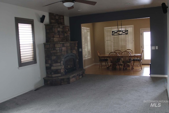 carpeted living area with a fireplace, ceiling fan, baseboards, and plenty of natural light