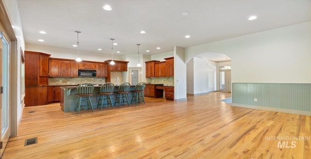 1563 W Colville Ct, Eagle, ID 83616 - kitchen with black microwave, arched walkways, a breakfast bar area, light wood-style flooring, and backsplash